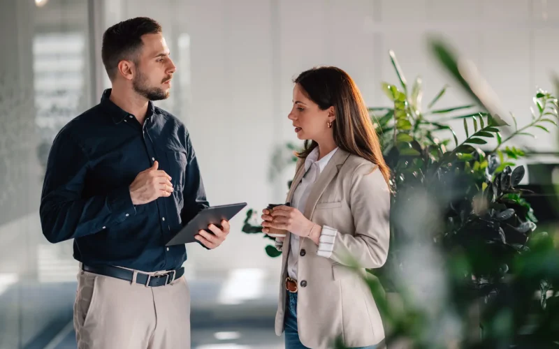 Focused managers standing at corporate office lobby with tablet in hands and talking about innovative business ideas. Portrait of successful businesspeople working as a team at enterprise office.