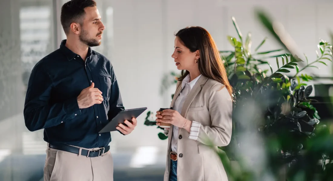 Focused managers standing at corporate office lobby with tablet in hands and talking about innovative business ideas. Portrait of successful businesspeople working as a team at enterprise office.